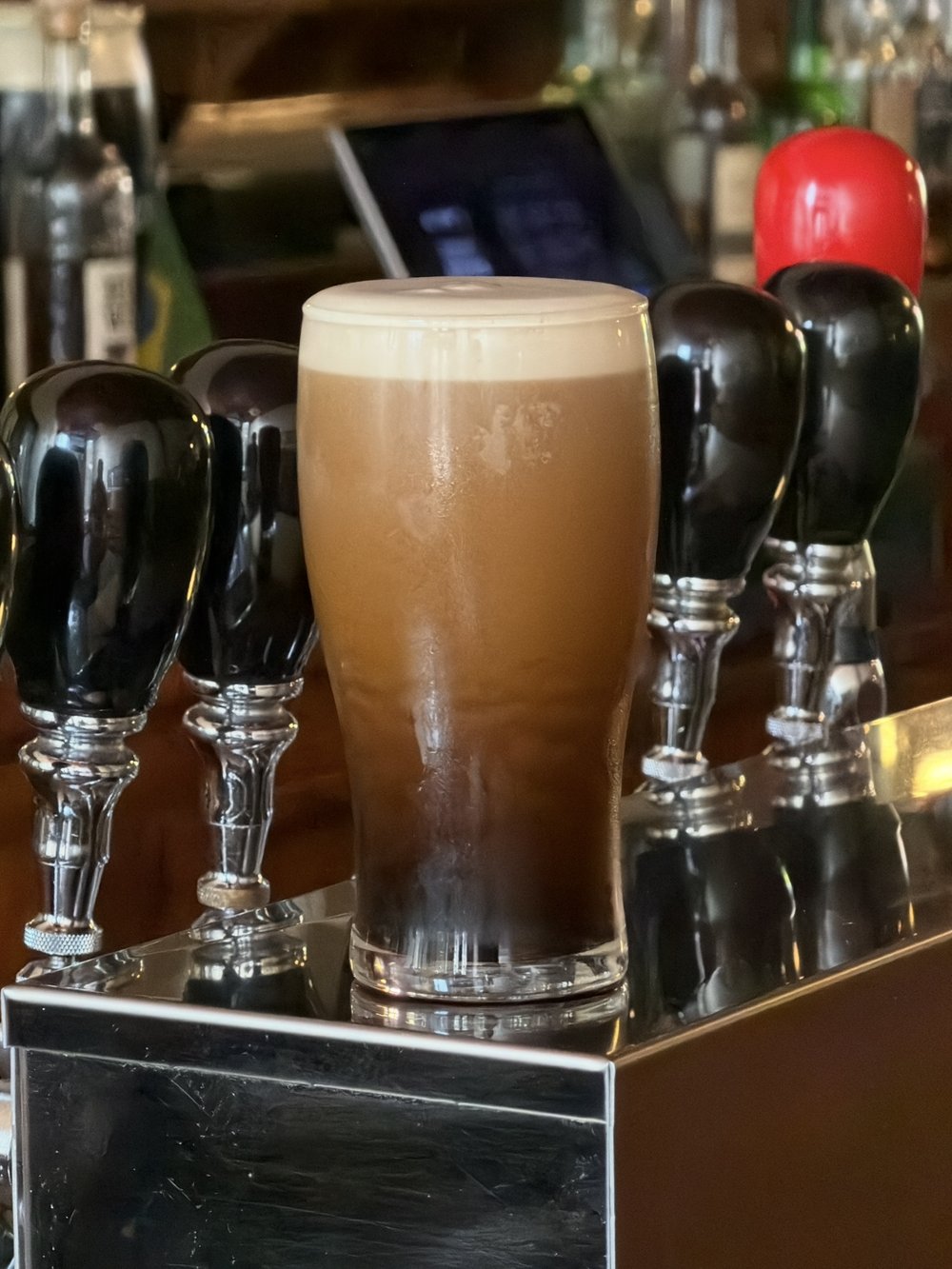A freshly poured pint of Guinness with a creamy head, standing between black tap handles on the bar